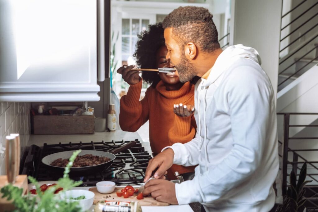 Um casal cozinha seu almoço de forma feliz, desfrutando de qualidade de vida no ambiente familiar.
