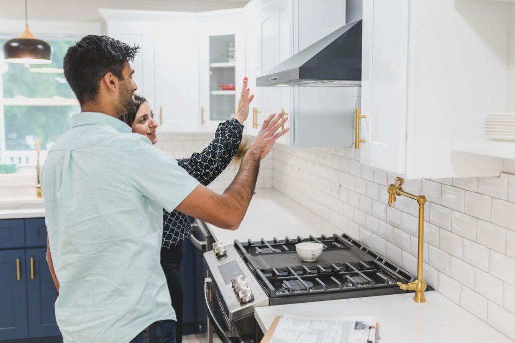 Na imagem uma agente imobiliária apresenta para um cliente detalhes da cozinha de um imóvel.
