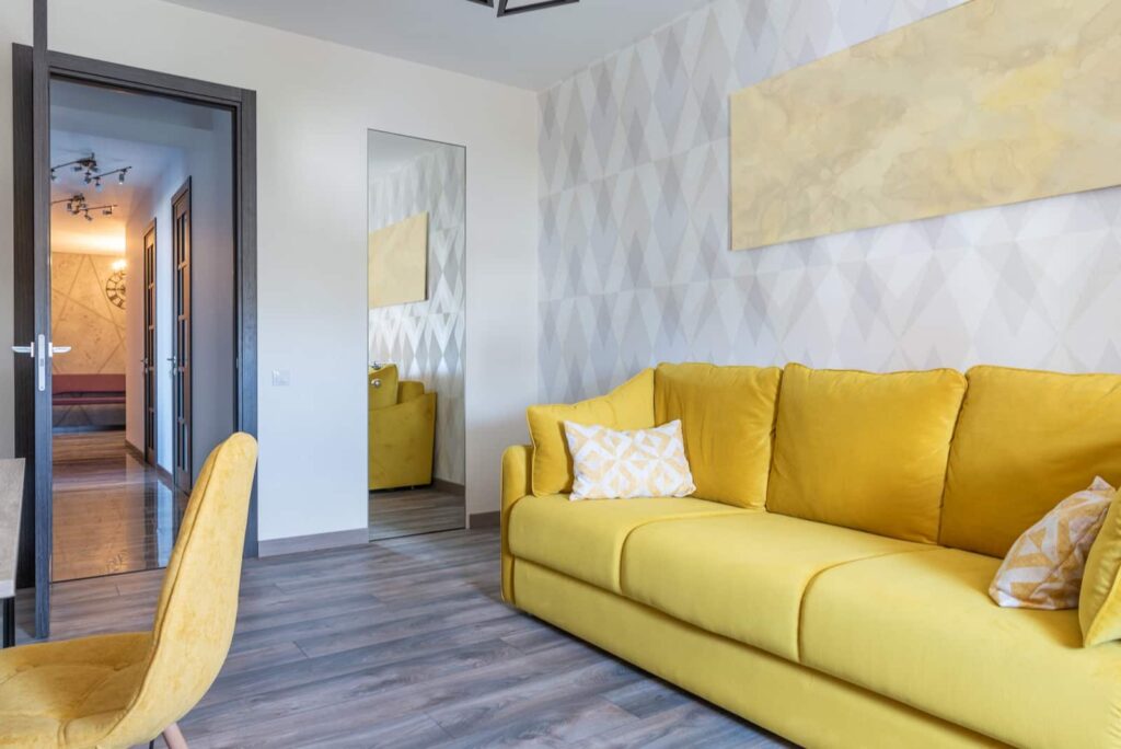 Um sofá amarelo com duas almofadas estampadas está sendo usado de exemplo de decoração contemporânea.
