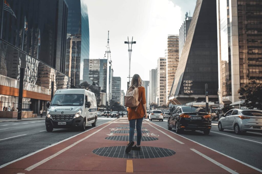 Uma mulher está caminhando por uma rua de São Paulo, um grande centro urbano.