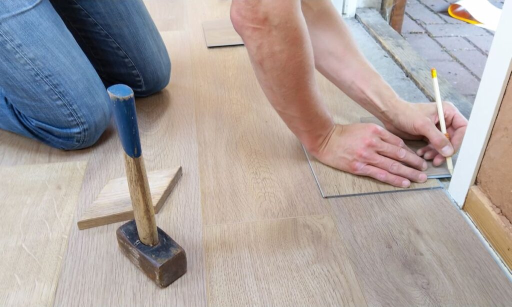 Uma pessoa está trabalhando em reparos residenciais trocando o piso do chão de uma sala.