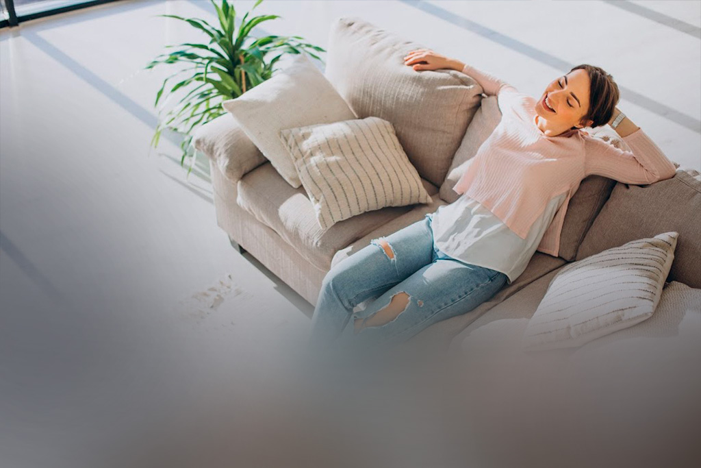 Uma mulher está sentada em seu sofá confortável, enquanto um robô aspirador aspira o tapete.