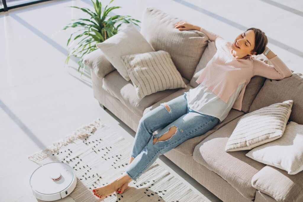 Uma mulher está sentada em seu sofá confortável, enquanto um robô aspirador aspira o tapete.